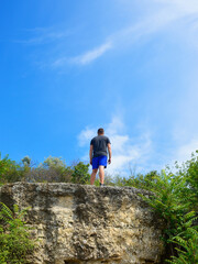 Successful hiker hiking on a mountain peak. Adventure composition with a man on top of a mountain cliff with a clear sky and white clouds in the background during sunset or sunrise