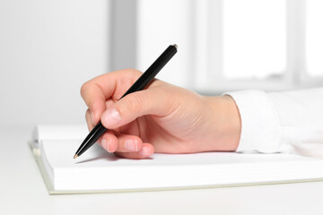Woman writing in notebook at white table in office, closeup