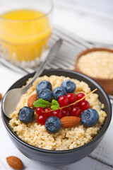 Bowl of delicious cooked quinoa with almonds, cranberries and blueberries on white wooden table, closeup