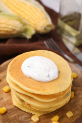 Tasty corn pancakes with sweet kernels and sauce served on wooden table, closeup