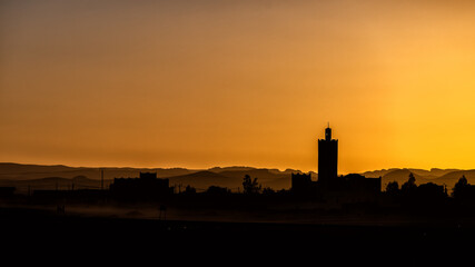 Silhouette of a typical Arab village with a mosque minaret at sunset. Ksar Tanamouste, Sahara, Morocco.