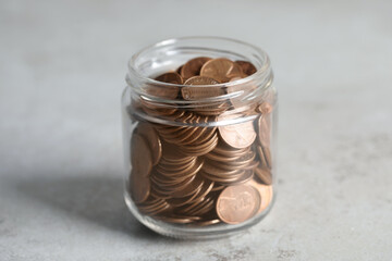 Glass jar with coins on light grey table, closeup