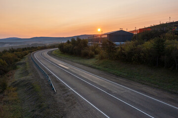 Morning aerial view of a highway. Empty road. Beautiful sunrise over an asphalt road. Road and transport infrastructure in Siberia and the Russian Far East. Kolyma highway, Magadan region, Russia.