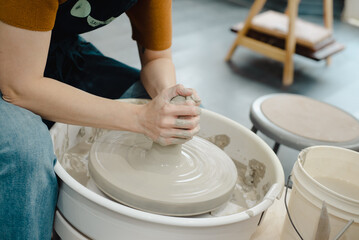 Closeup of potter hands working on pottery wheel in ceramic studio with clay hands side view with pottery wheel in motion 