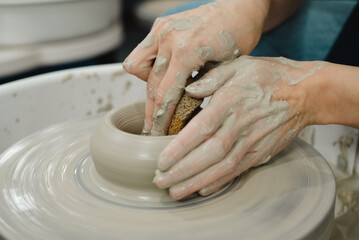 Closeup of potter hands working on pottery wheel in ceramic studio with clay hands side view with pottery wheel in motion