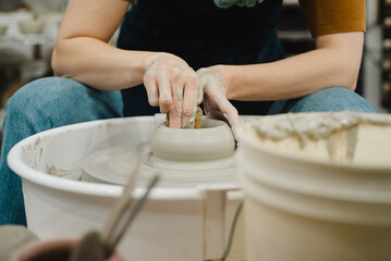 Closeup of potter hands working on pottery wheel in ceramic studio with clay hands front view with pottery wheel in motion
