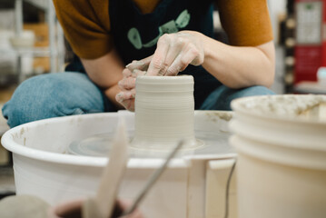 Potter hands closeup working on pottery wheel using sponge on cup in ceramic studio creating ceramic ware front view of potter bent over