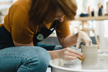Potter hands closeup working on pottery wheel using sponge on cup in ceramic studio creating ceramic ware side view of potter bent over