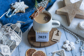 A cup of hot coffee, zifirki, sweets and Christmas decorations on a wooden table. Calendar for New Year 2023.