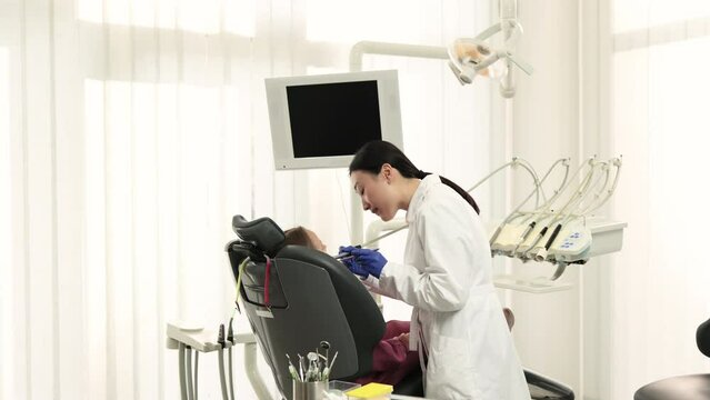 Beautiful smile with white teeth. Asian dentist treating teeth of a young beautiful girl using tooth drill through a magnifying glass in the dental office.