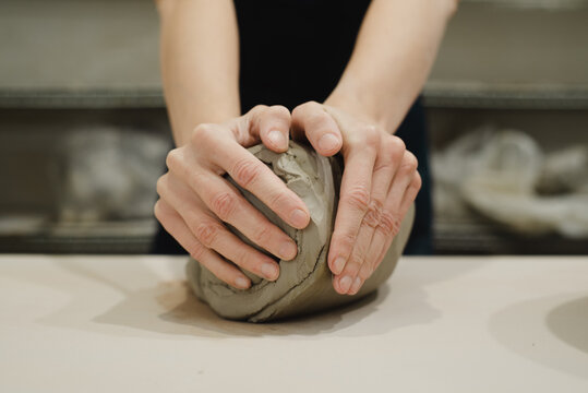 Potter spiral wedging large block of clay on canvas table ready for pottery wheel. Closeup of potter hands.