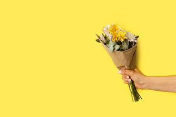 Mano de mujer sosteniendo una ramo de flores naturales sobre un fondo amarillo liso y aislado....
