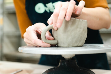 Hands of a potter attaching handle to pinch pot cup in ceramic studio pottery workshop