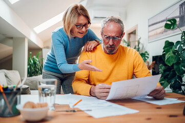 Senior couple sitting at table and looking into blueprints of their new home