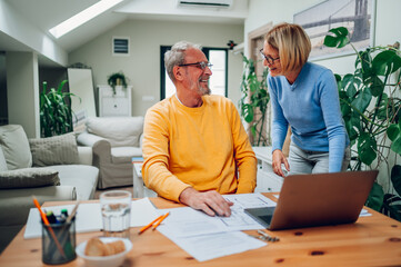 Senior couple sitting at table and looking into blueprints of their new home