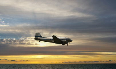 A turboprop aircraft flies over the sea at sunset.