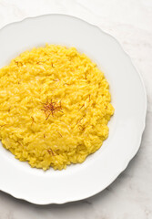 Close-up of risotto alla Milanese in a white aristocratic dish on the red terracotta background. A classic recipe for Lombard risotto with saffron for the cold season. Cuisine of the north Italy 
