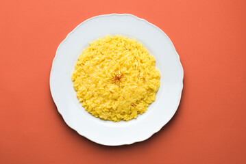 Risotto alla Milanese in a white aristocratic dish on the red terracotta background. A classic recipe for Lombard risotto with saffron for the cold season. Cuisine of the north Italy 