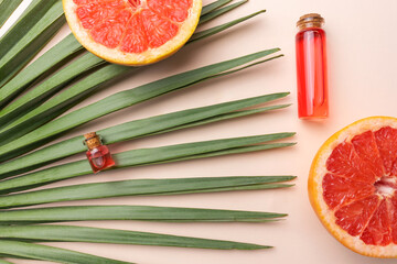 Essential citrus oil on a tropical palm leaf in transparent glass bottles top view on beige background.