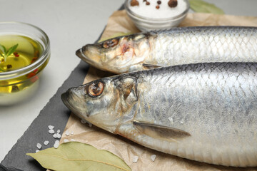 Slate plate with salted herrings, oil and spices on grey table, closeup