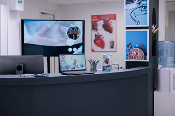 Front desk of medical clinic reception area with informative posters, office supplies and computers. Laptop on hospital waiting area counter showing female general practitioner.