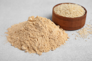 Sesame flour and wooden bowl of seeds on light grey table