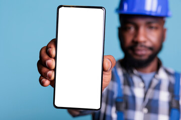 Professional man holding smartphone with white screen display in studio, using work uniform and...