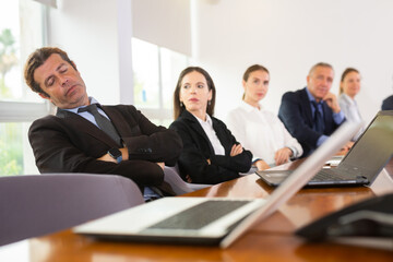 Tired middle aged mature white businessman in formal suit napping during corporate team meeting...
