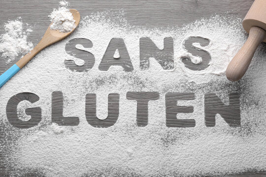 Words Sans gluten written with flour and different kitchen utensils on wooden table, flat lay