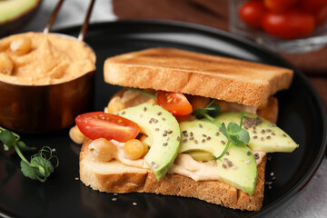 Delicious sandwich with hummus and vegetables on black plate, closeup