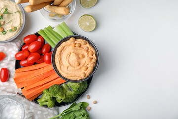 Plate with delicious hummus and fresh vegetables on white table, flat lay. Space for text