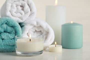 Beautiful spa composition with burning candles and rolled towels on white table, closeup