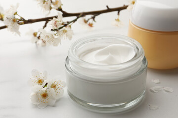 Obraz na płótnie Canvas Jars of face cream and flowers on white marble table