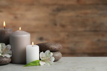 Beautiful composition with burning candles, spa stones and flowers on light grey table. Space for text