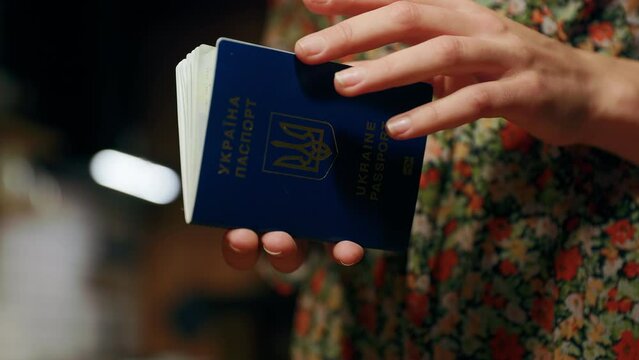 Female refugee's hands opening and closing a Ukrainian passport with many traveling stamps inside