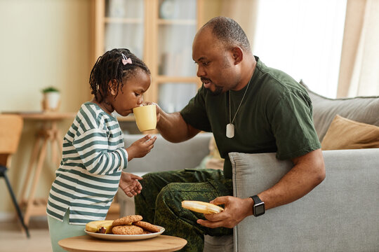 Side view portrait of caring black father sharing tea and cookies with cute daughter