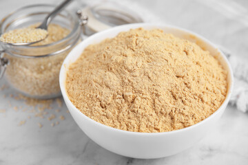 Sesame flour in ceramic bowl on white marble table, closeup