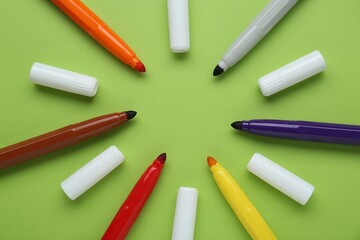 Many different colorful markers and caps on light green background, flat lay