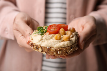 Woman holding delicious sandwich with hummus , tomato slices and chickpeas , closeup
