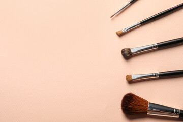 Different makeup brushes on light beige background, flat lay . Space for text