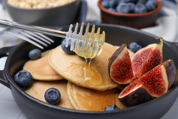 Pouring honey onto tasty oatmeal pancakes, closeup