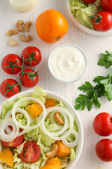 Bowl of delicious salad with Chinese cabbage and different ingredients on white wooden table, flat lay