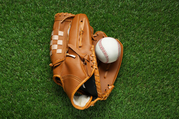 Catcher's mitt and baseball ball on green grass, top view. Sports game