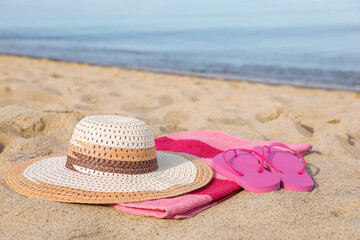 Beach towel with straw hat and slippers on sand near sea