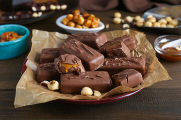 Many tasty chocolate bars and nuts on wooden table, closeup