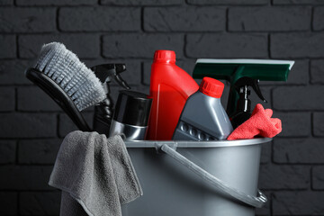 Different car cleaning products in bucket near black brick wall, closeup