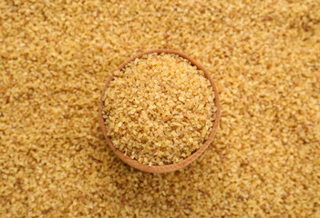 Wooden bowl on pile of uncooked bulgur, top view
