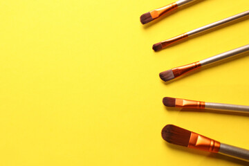 Different makeup brushes on yellow background, flat lay. Space for text