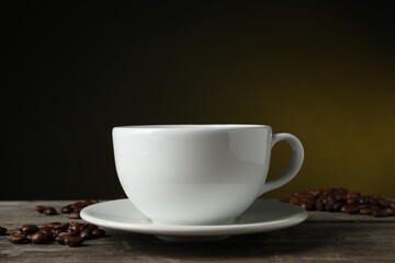 Cup of hot aromatic coffee and roasted beans on wooden table