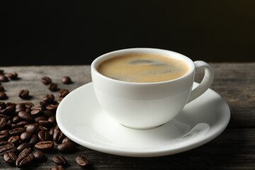 Cup of hot aromatic coffee and roasted beans on wooden table against dark background